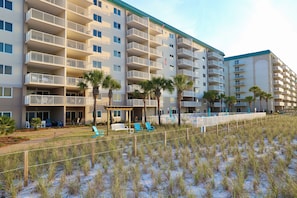 Ein mehrstöckiges Hotel mit Balkonen, Sitzgelegenheiten im Freien und einer Sandstrand-Anlage.
