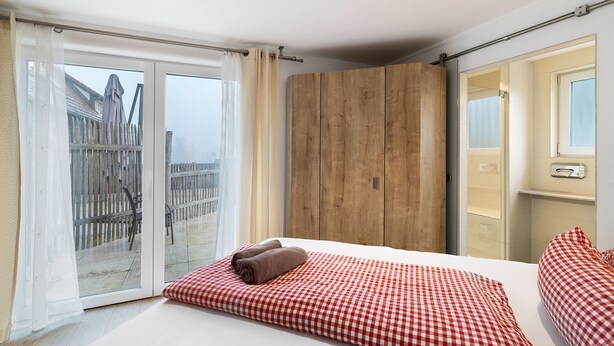 Quarto com uma cama grande, um guarda-roupa de madeira e uma porta de vidro deslizante para uma varanda.