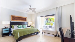 Une chambre avec un lit, des tables de chevet, une télévision et un balcon donnant sur un espace verdoyant.