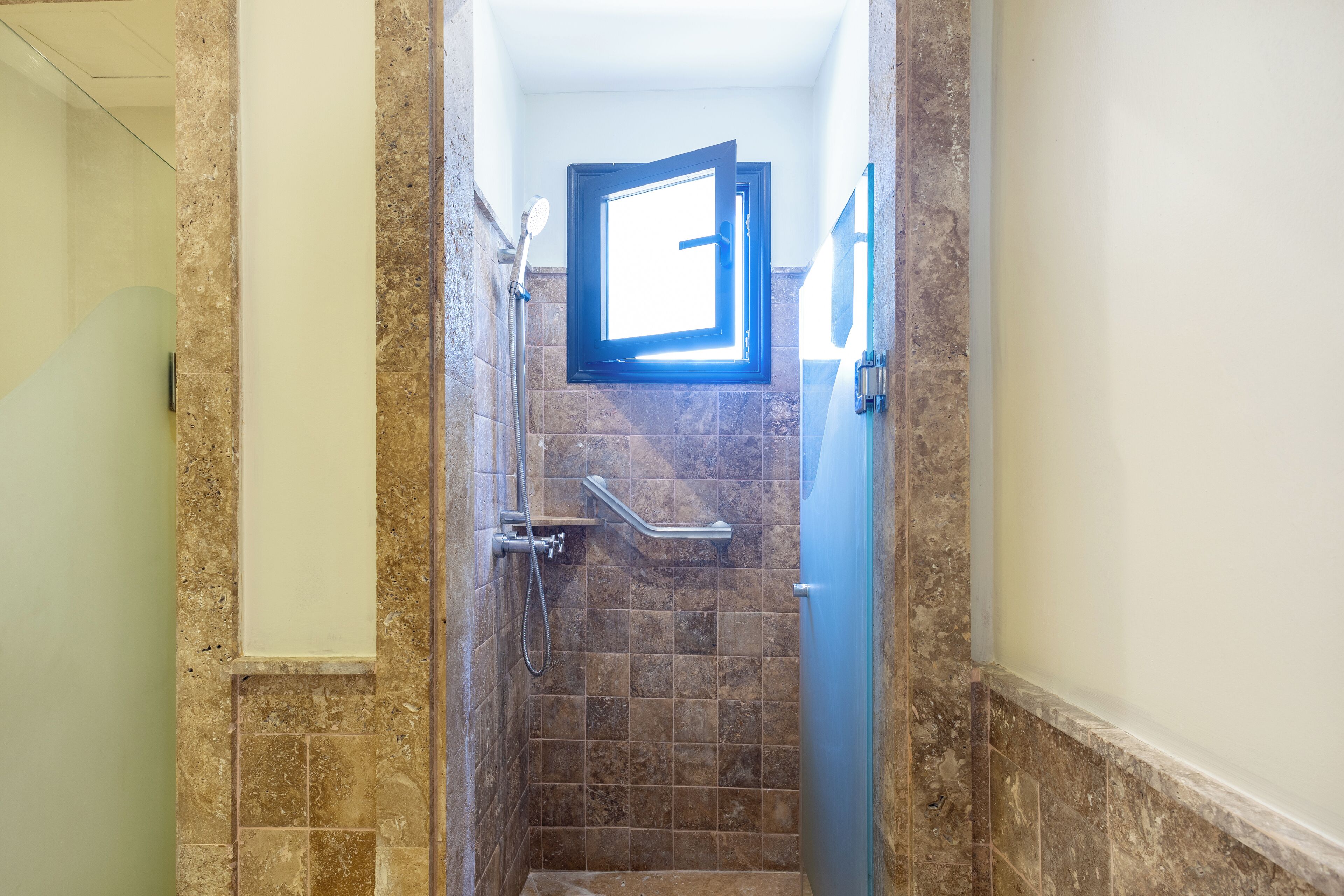 A bathroom with a shower, a glass door, and a window.
