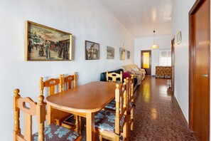 A dining area with a wooden table and chairs, a sofa, and a hallway leading to a bedroom.