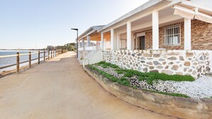A coastal building with a stone facade, a concrete pathway, and a wooden railing along the water.