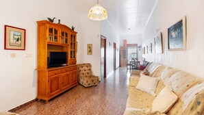 A living room with a wooden entertainment center, a floral armchair, a sofa with cushions, and a hanging light fixture.