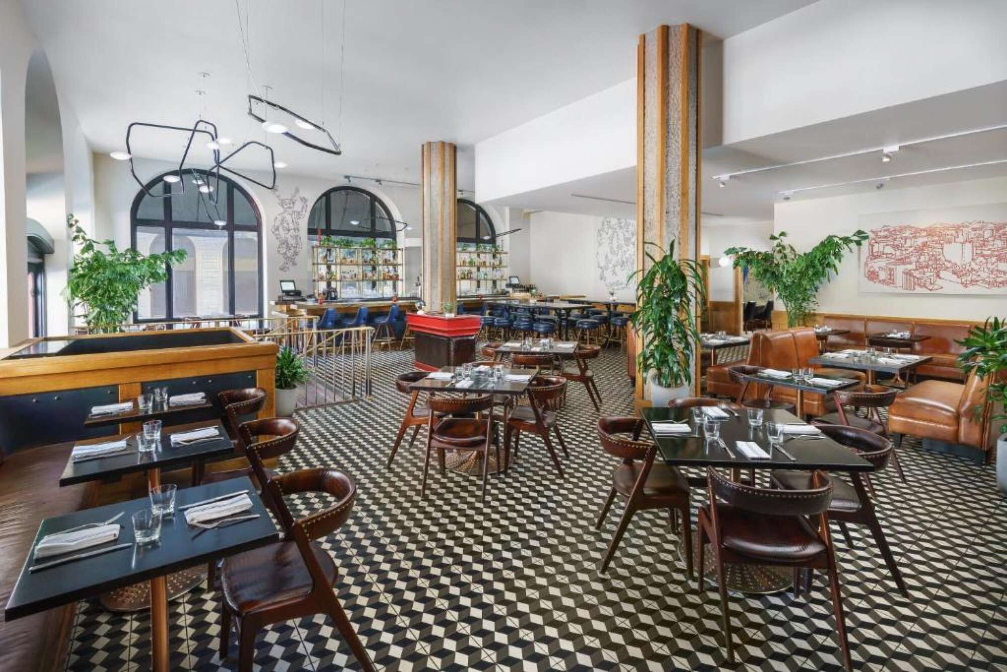 Een ruim restaurant met hoge plafonds, zwart-wit geruit vloer en diverse zithoeken, waaronder zitjes en tafels.