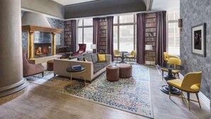 A spacious living room with a fireplace, a sofa set, a coffee table, and a bookshelf. - Union Square Stay | Bar. Restaurant + Gym (San Francisco)