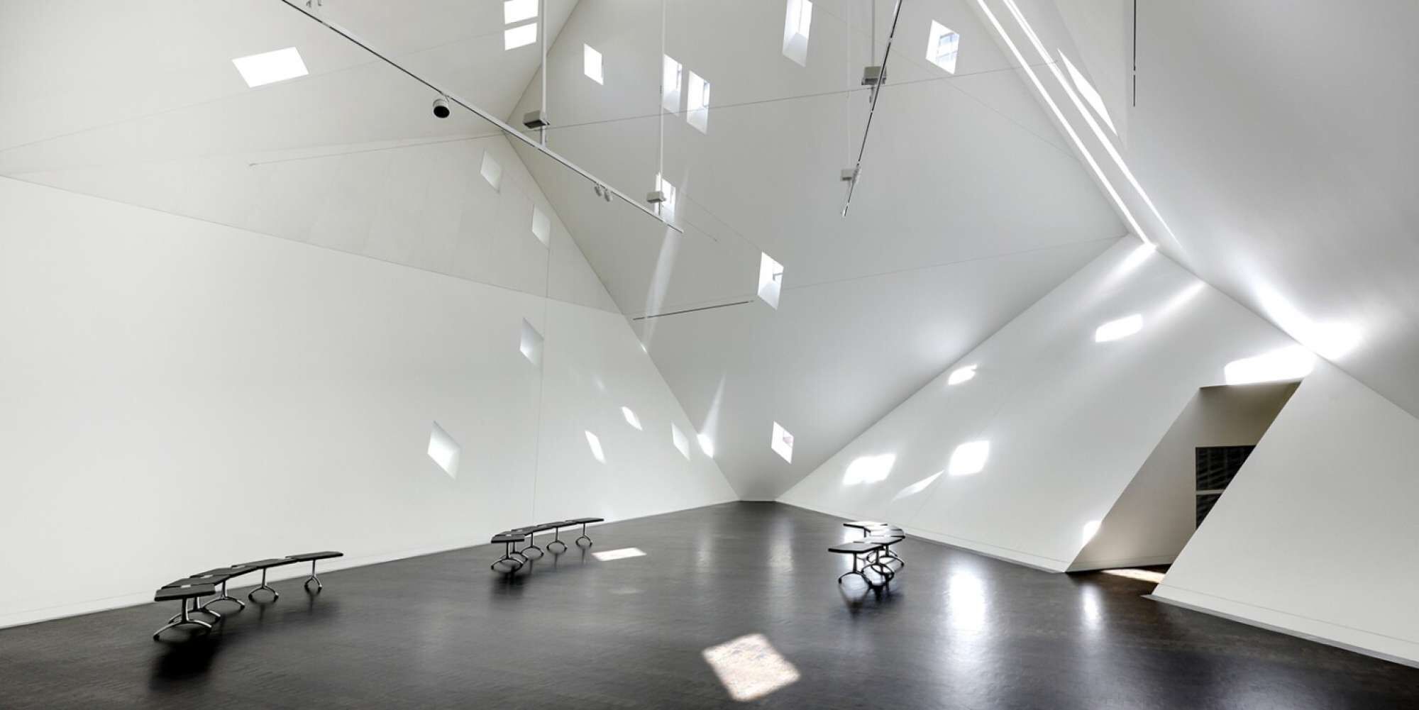 Ein geräumiges, modernes Interieur mit geometrischen Wänden und Decken, minimalistischer Einrichtung und natürlichem Licht.