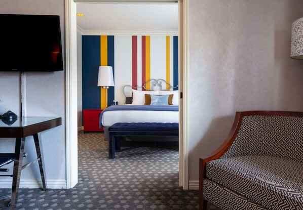 A hotel room with a bed, a desk, a TV, and a patterned armchair. - Near Powell Cable Car | Italian Dining + Fitness (San Francisco)