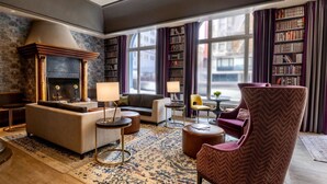 A modern living room with a fireplace, sofas, a coffee table, and a large window with bookshelves. - Near Powell Cable Car | Italian Dining + Fitness (San Francisco)