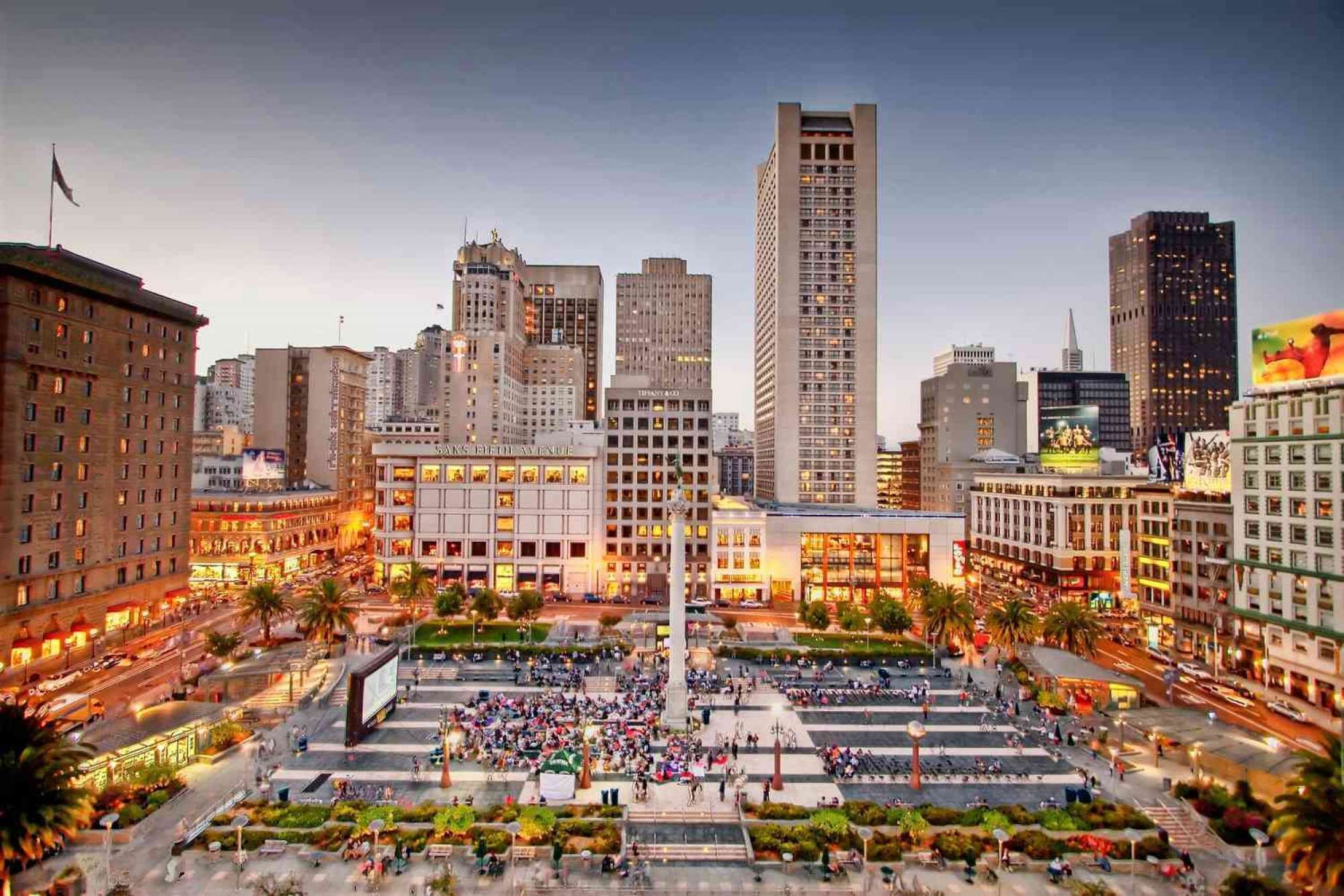 A cityscape with a prominent skyscraper, a central plaza with a fountain, and surrounding buildings with illuminated windows.