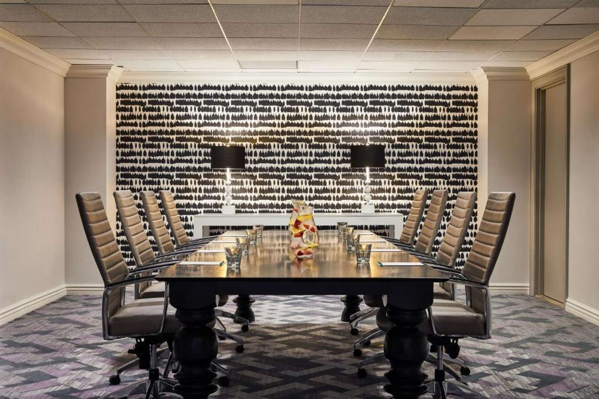 A conference room with a long table, multiple chairs, and a patterned wall.