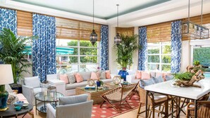 A spacious living room with a sofa set, a dining table, and a large window with blue patterned curtains. - Steps to Miami Beach + On-site Dining. Pool. Bikes (Miami Beach)
