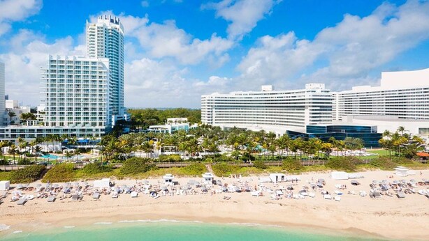 A beachfront hotel with multiple high-rise buildings, a sandy beach, and a pool area. - Steps to Miami Beach + On-site Dining. Pool. Bikes (Miami Beach)