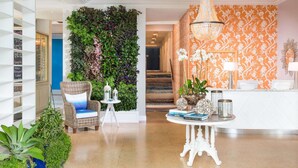 A lobby with a green vertical garden, a wicker chair with a blue cushion, a white round table with books and decorative items, and an orange patterned wall. - Steps to Miami Beach + On-site Dining. Pool. Bikes (Miami Beach)