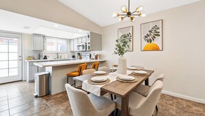 Una cocina moderna con comedor, que cuenta con una isla central, armarios blancos y una lámpara de araña.