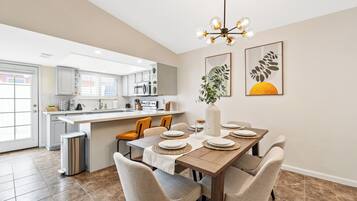 Une cuisine moderne avec un coin repas, comprenant un îlot central, des meubles blancs et un lustre.