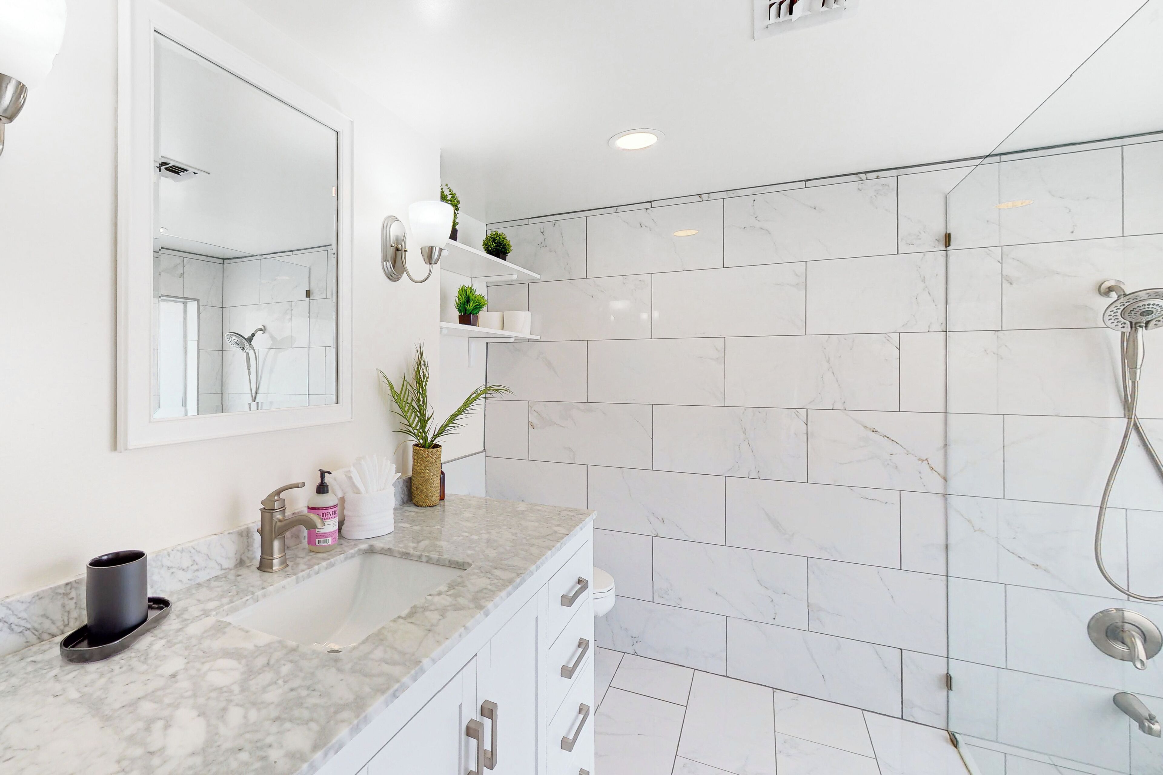 A modern bathroom with a marble sink, a large mirror, a shower, and a toilet.