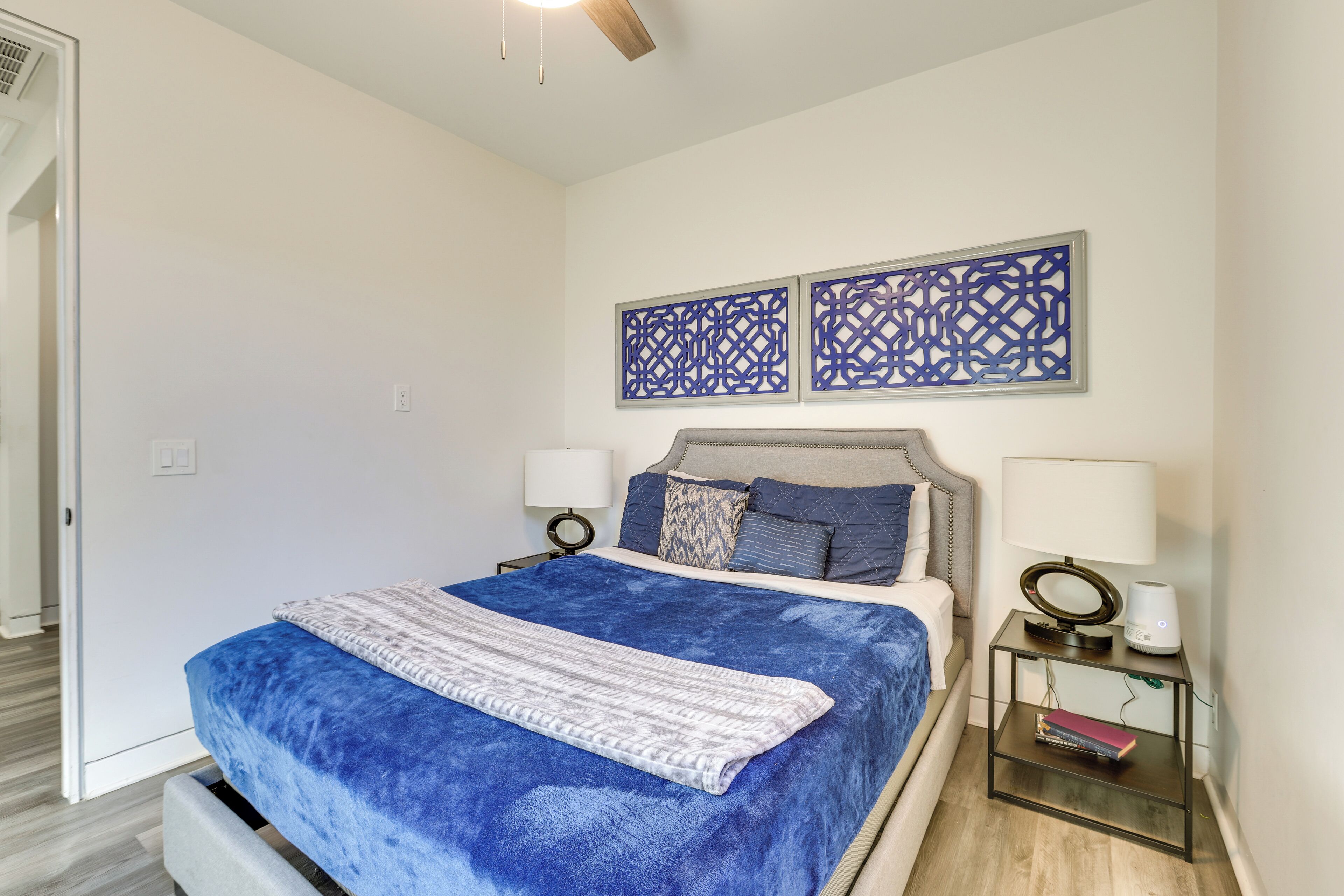 A bedroom with a bed, two bedside tables with lamps, a wall-mounted decorative panel, and a door.