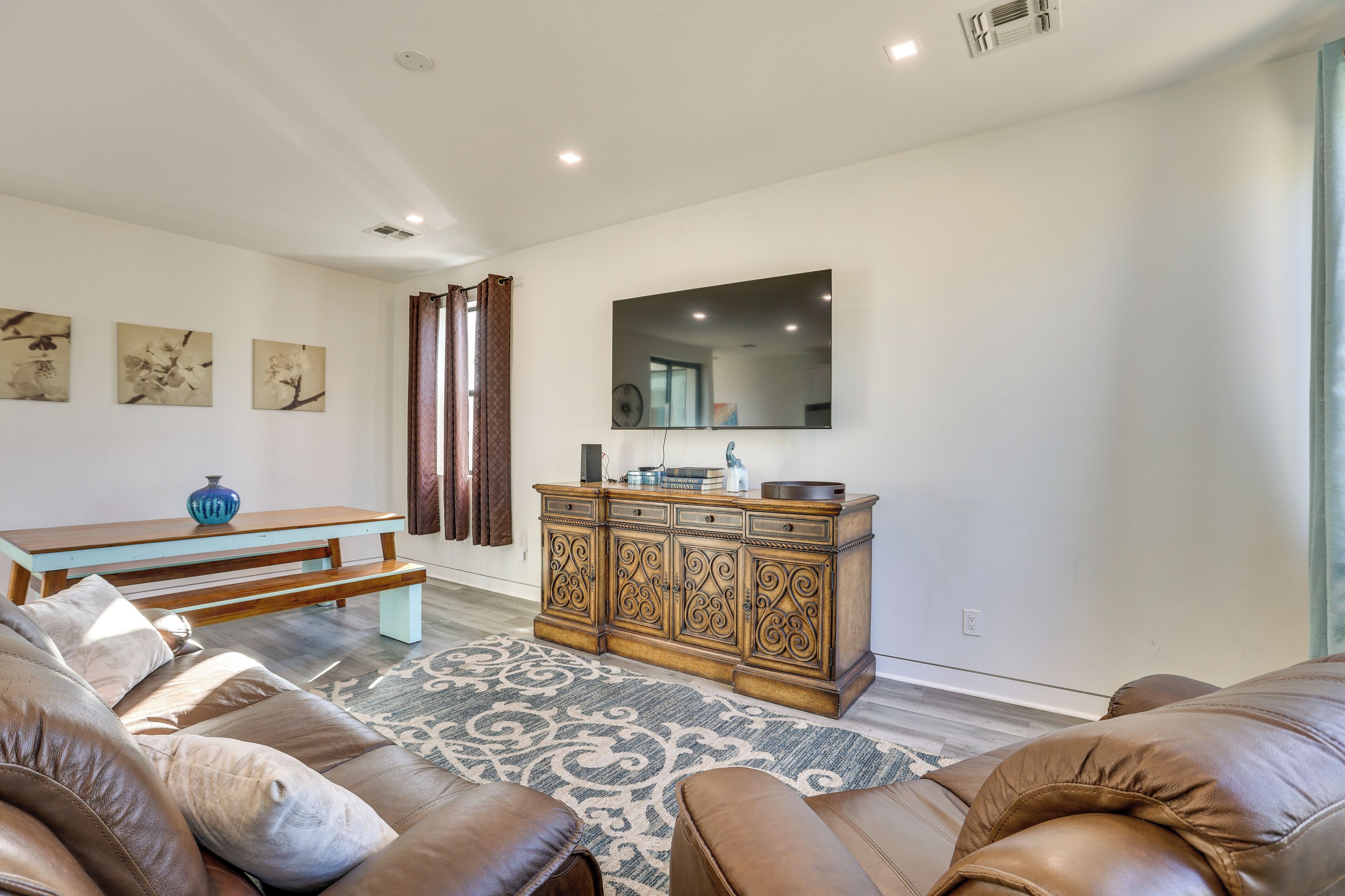 A living room with a brown leather sofa, a wooden bench, a patterned rug, a wooden cabinet, and a large mirror on the wall.