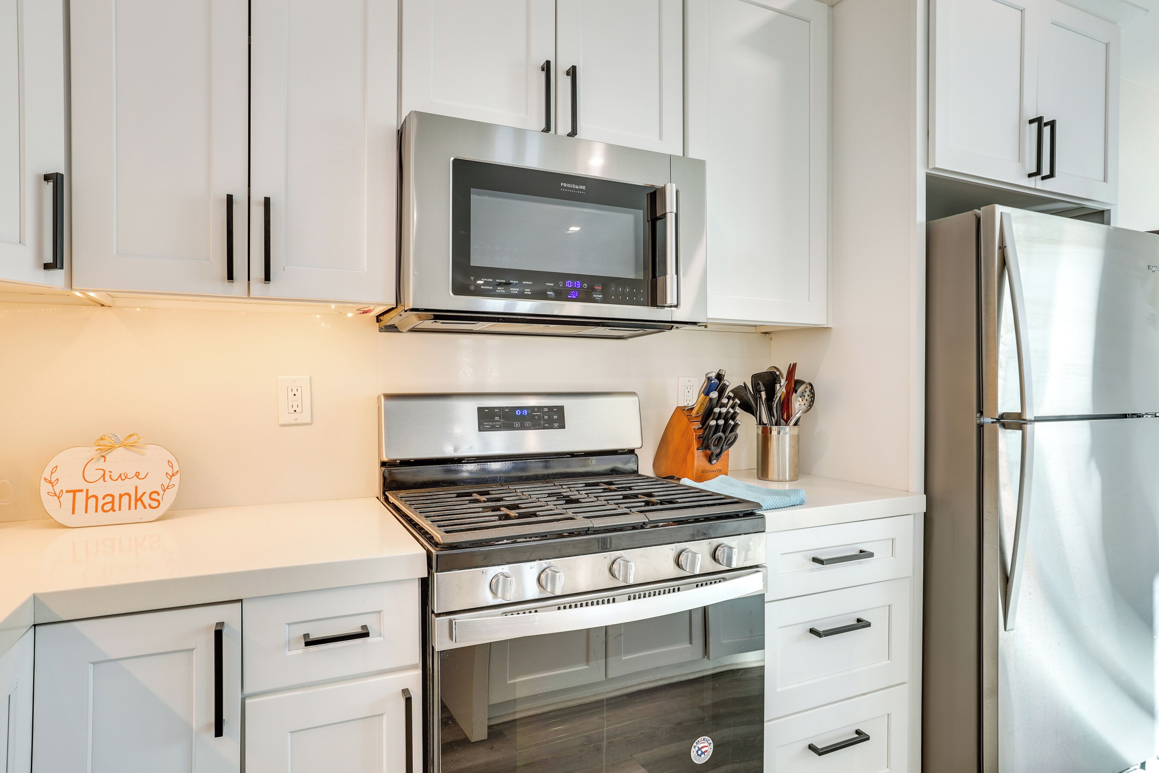 Une cuisine moderne avec des meubles blancs, une cuisinière en acier inoxydable, un four à micro-ondes et un réfrigérateur.