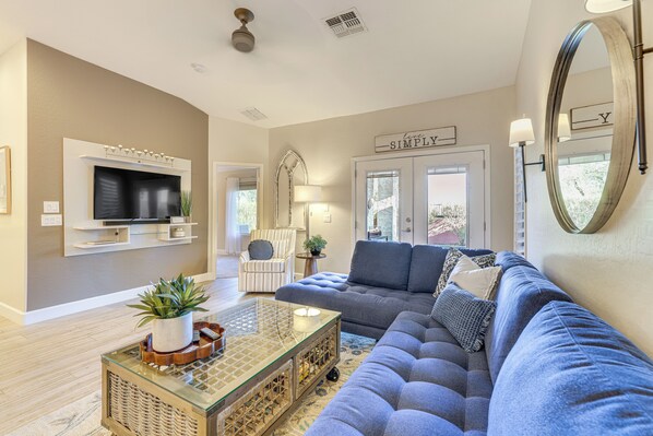 A living room with a large gray sectional sofa, a glass coffee table, and a flat-screen TV mounted on the wall. There is a mirror on the wall and a sign that reads "SIMPLY." - < 1 Mi to Golf: Charming Ahwatukee Foothills Villa (Phoenix)