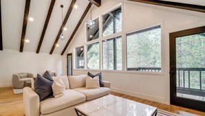 A spacious living room with a beige sectional sofa, a marble coffee table, and large windows offering a view of trees. - Walk to Gondola: Truckee Retreat w/ Resort Perks! (Truckee)
