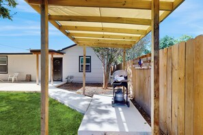 A backyard with a wooden pergola, a grill, and a white house in the background. - 4BR Cozy House w/ Kitchen & Great Location (San Antonio)