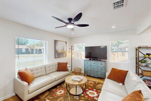 A living room with a sofa, a coffee table, a TV, and a ceiling fan. - 4BR Cozy House w/ Kitchen & Great Location (San Antonio)