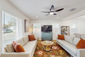 A living room with a sofa set, a coffee table, a TV, and a ceiling fan. - 4BR Cozy House w/ Kitchen & Great Location (San Antonio)