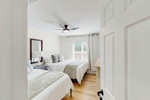 A bedroom with two beds, a ceiling fan, a window with blinds, and a nightstand with a lamp. - 4BR Cozy House w/ Kitchen & Great Location (San Antonio)