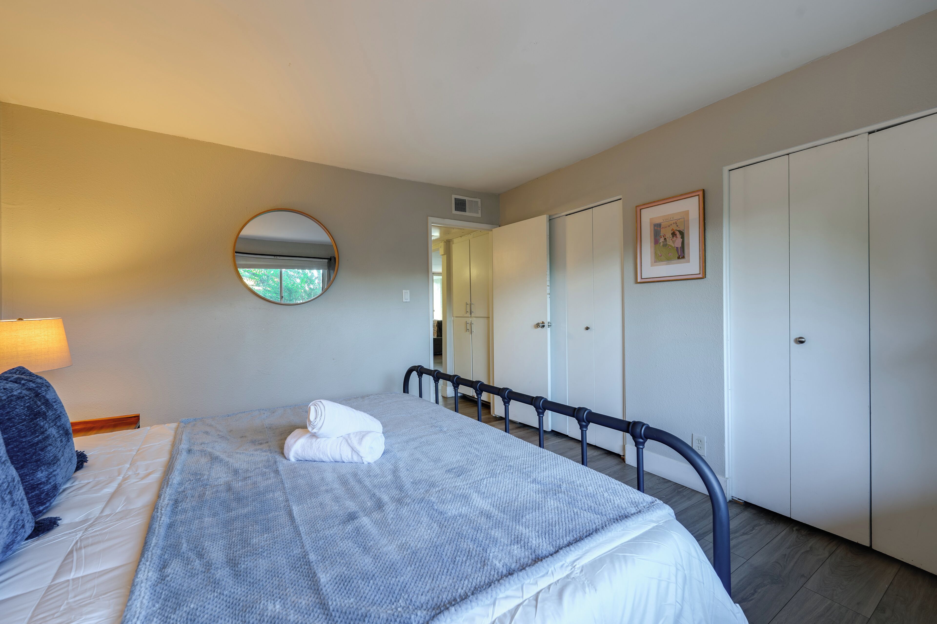 Een slaapkamer met een bed, een ronde spiegel, een kledingkast en een ingelijst schilderij aan de muur.