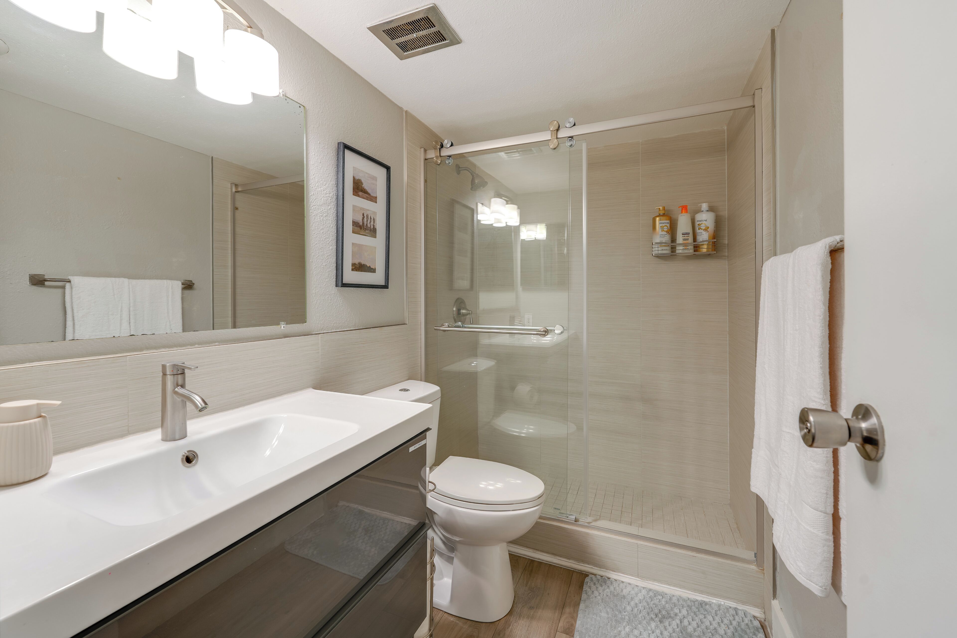 A modern bathroom with a white sink, toilet, and glass-enclosed shower.
