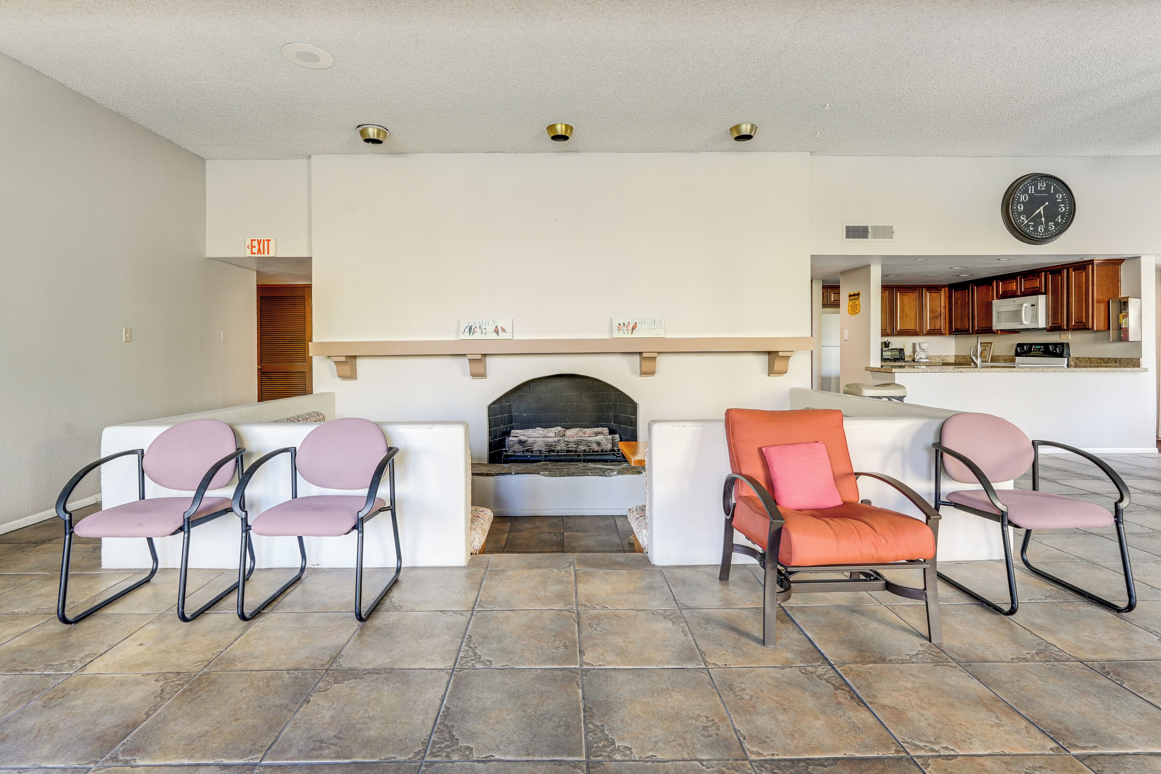 A living room with a fireplace, seating area, and kitchen in the background.
