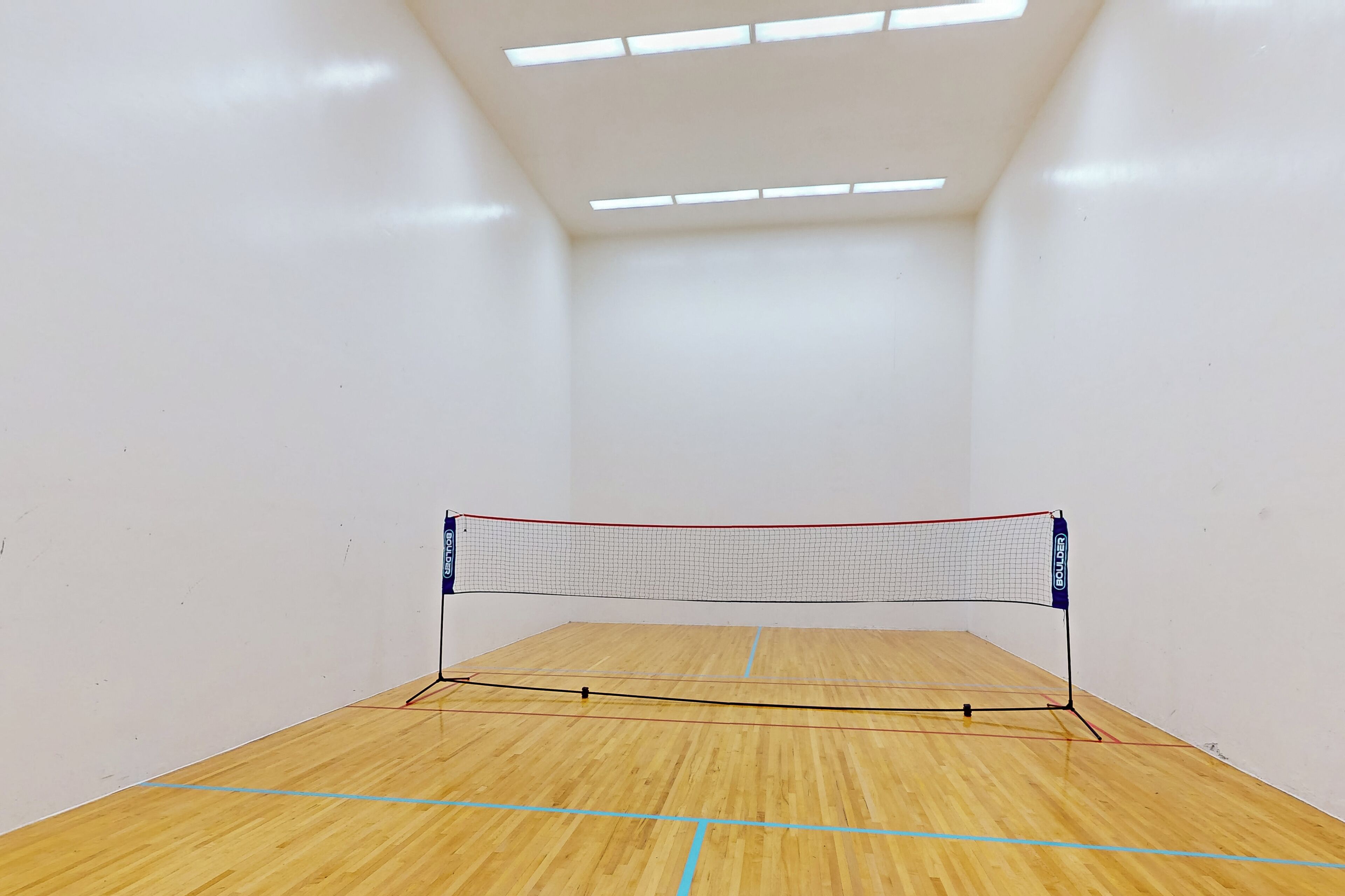 A squash court with a net, wooden floor, and white walls.