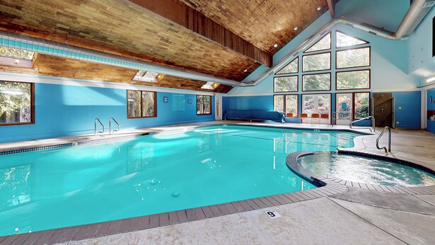 A large indoor swimming pool with a wooden ceiling and large windows.