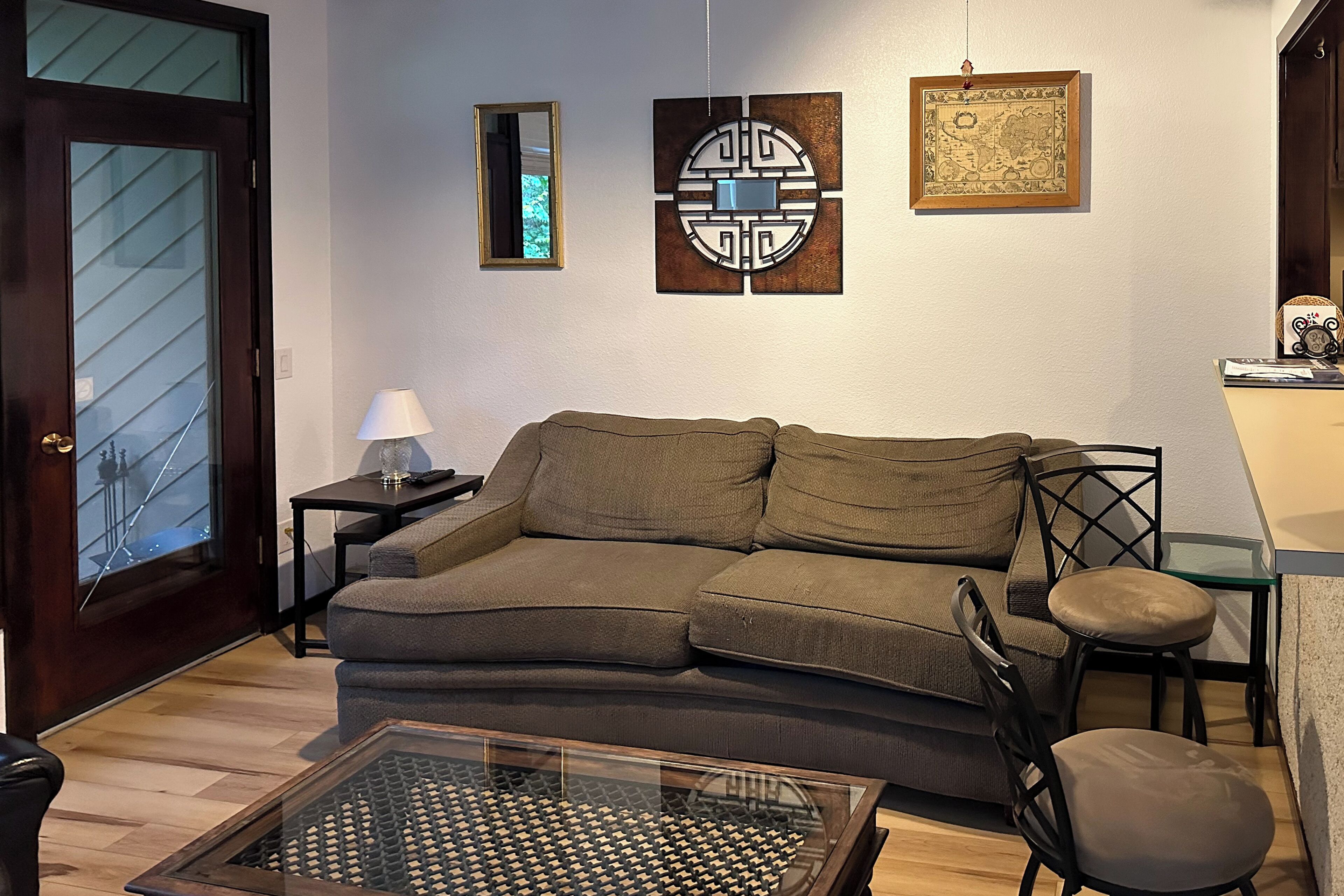 A living room with a brown sofa, a glass coffee table, a lamp, and artwork on the wall.