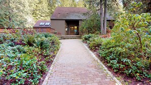A rustic cabin with a brick pathway leading to the entrance, surrounded by dense forest.