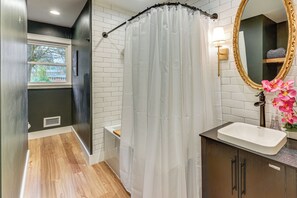 Ein Badezimmer mit Duschvorhang, Waschbecken mit Spiegel und einem Fenster mit Blick auf Gebäude.