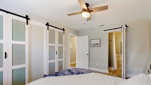 A bedroom with a bed, a ceiling fan, and a door leading to a bathroom. - Cozy Duplex Spacious Close to Everything (Pensacola)