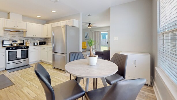 A modern kitchen with white cabinets, stainless steel appliances, and a round dining table with chairs. - Cozy Duplex Spacious Close to Everything (Pensacola)
