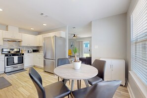 A modern kitchen with white cabinets, stainless steel appliances, and a round dining table with chairs. - Cozy Duplex Spacious Close to Everything (Pensacola)