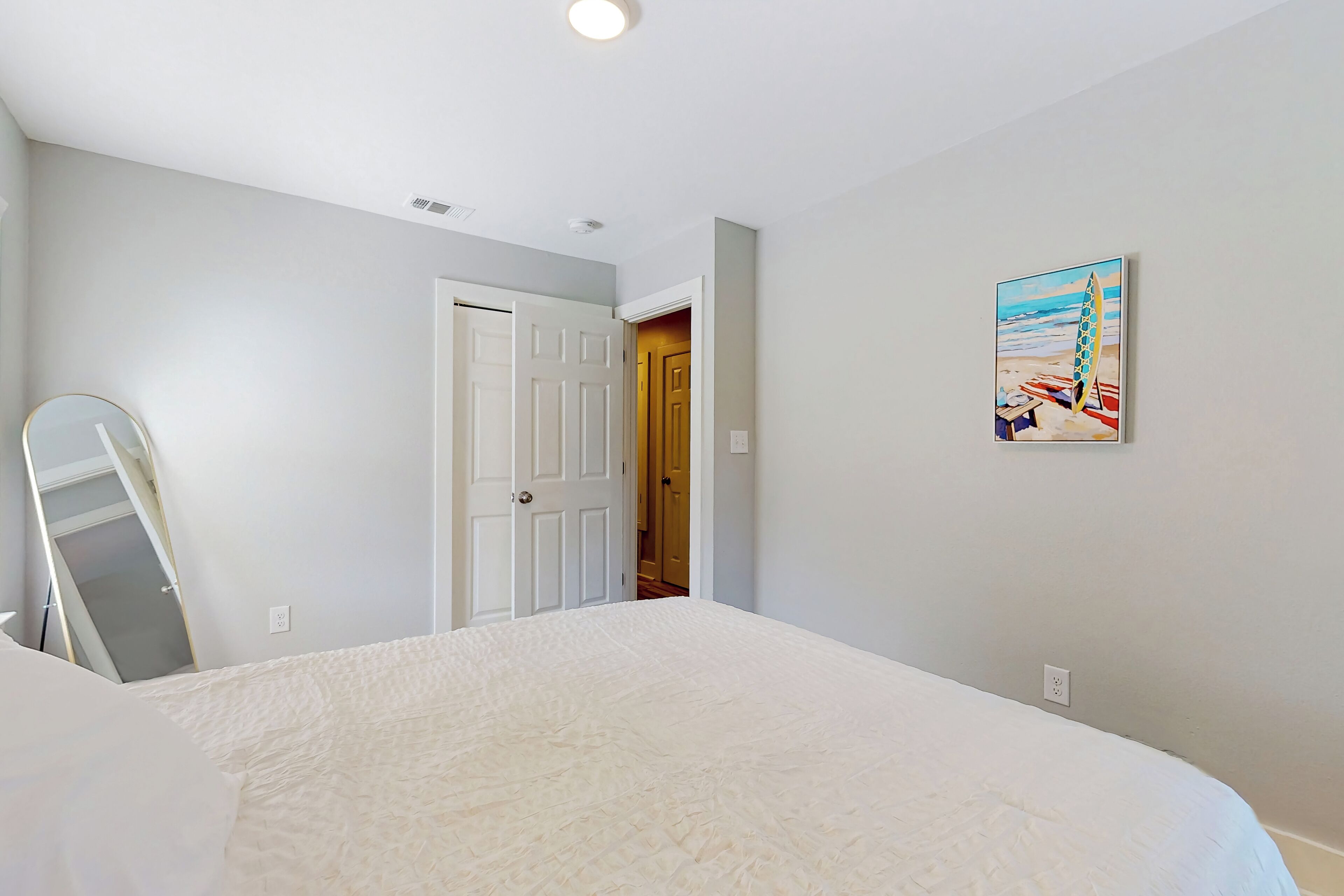 A bedroom with a bed, a door, and a painting of a beach scene.