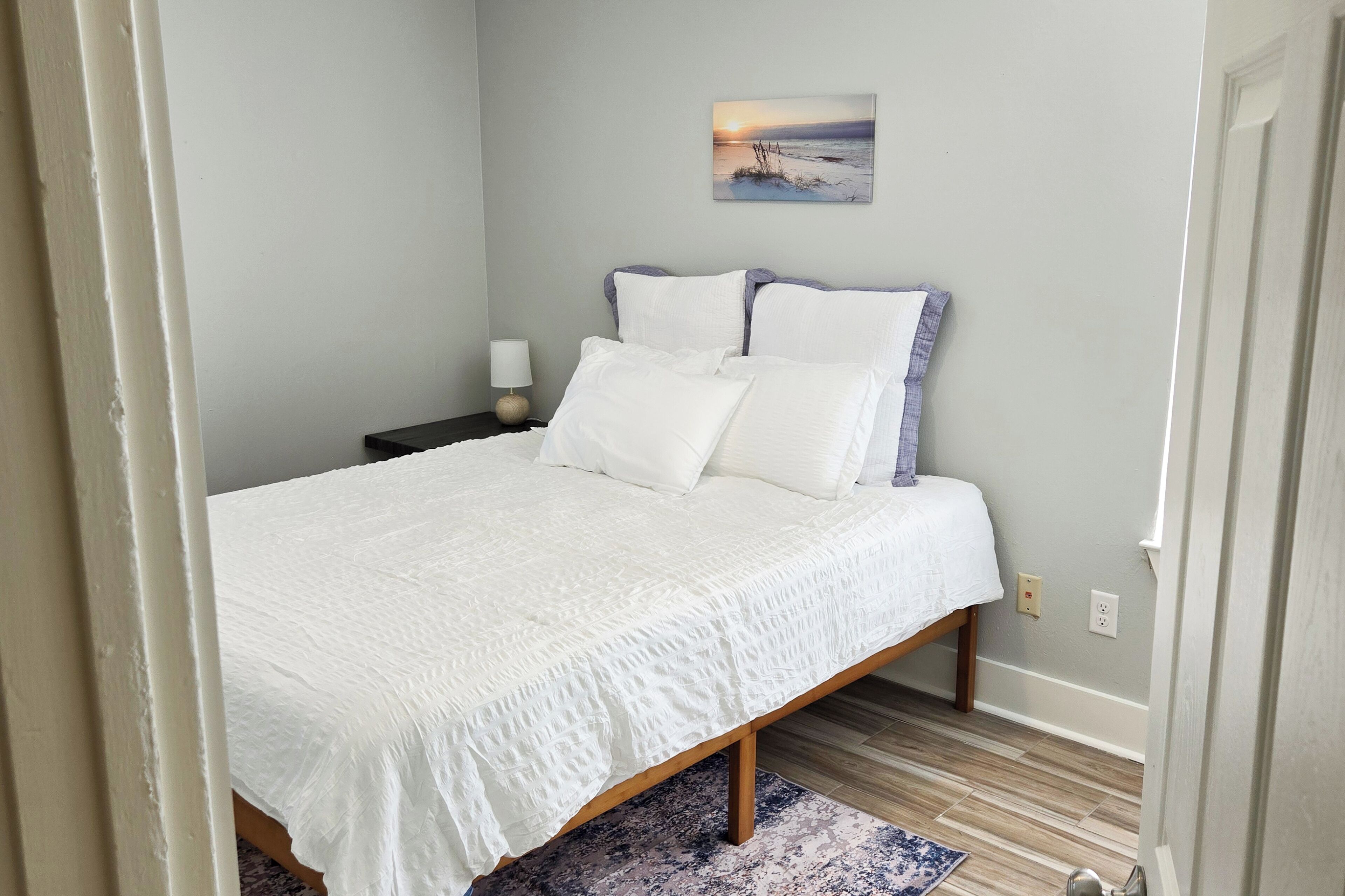 Un dormitorio con cama, mesita de noche, lámpara y un cuadro en la pared.