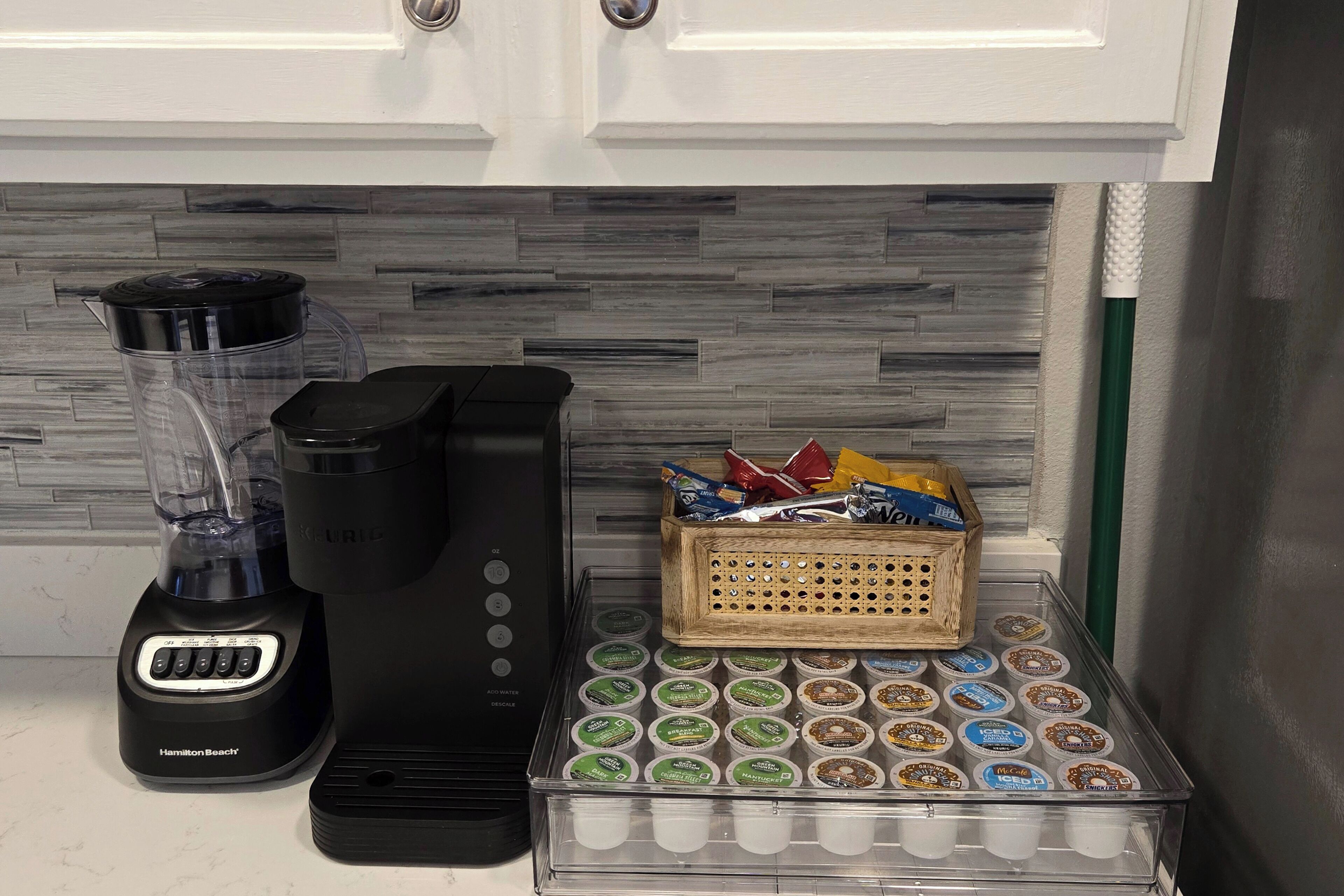 A kitchen counter with a Hamilton Beach blender, a coffee maker, and a container of yogurt cups.