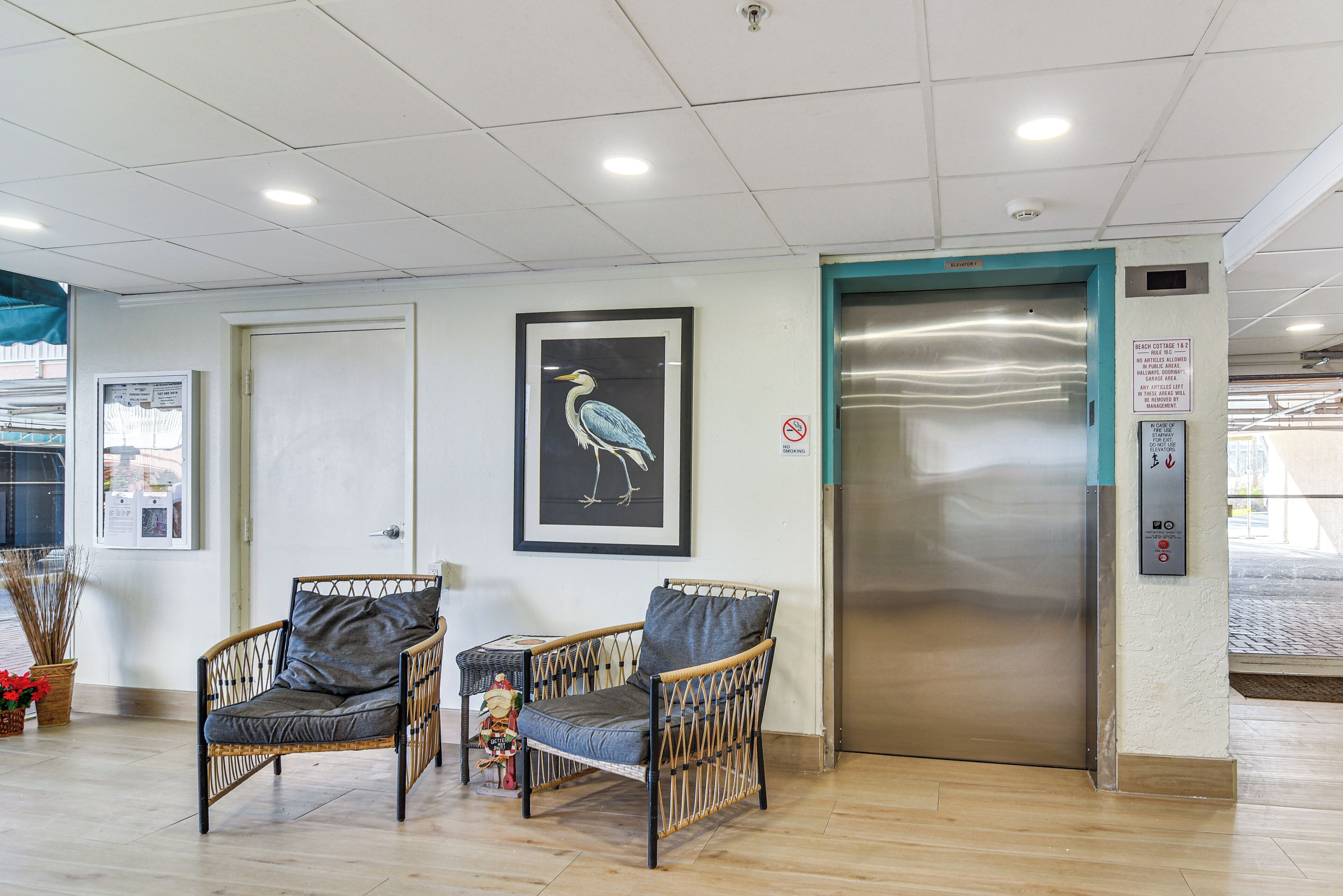 A lobby with wicker chairs, a framed bird artwork, and an elevator.