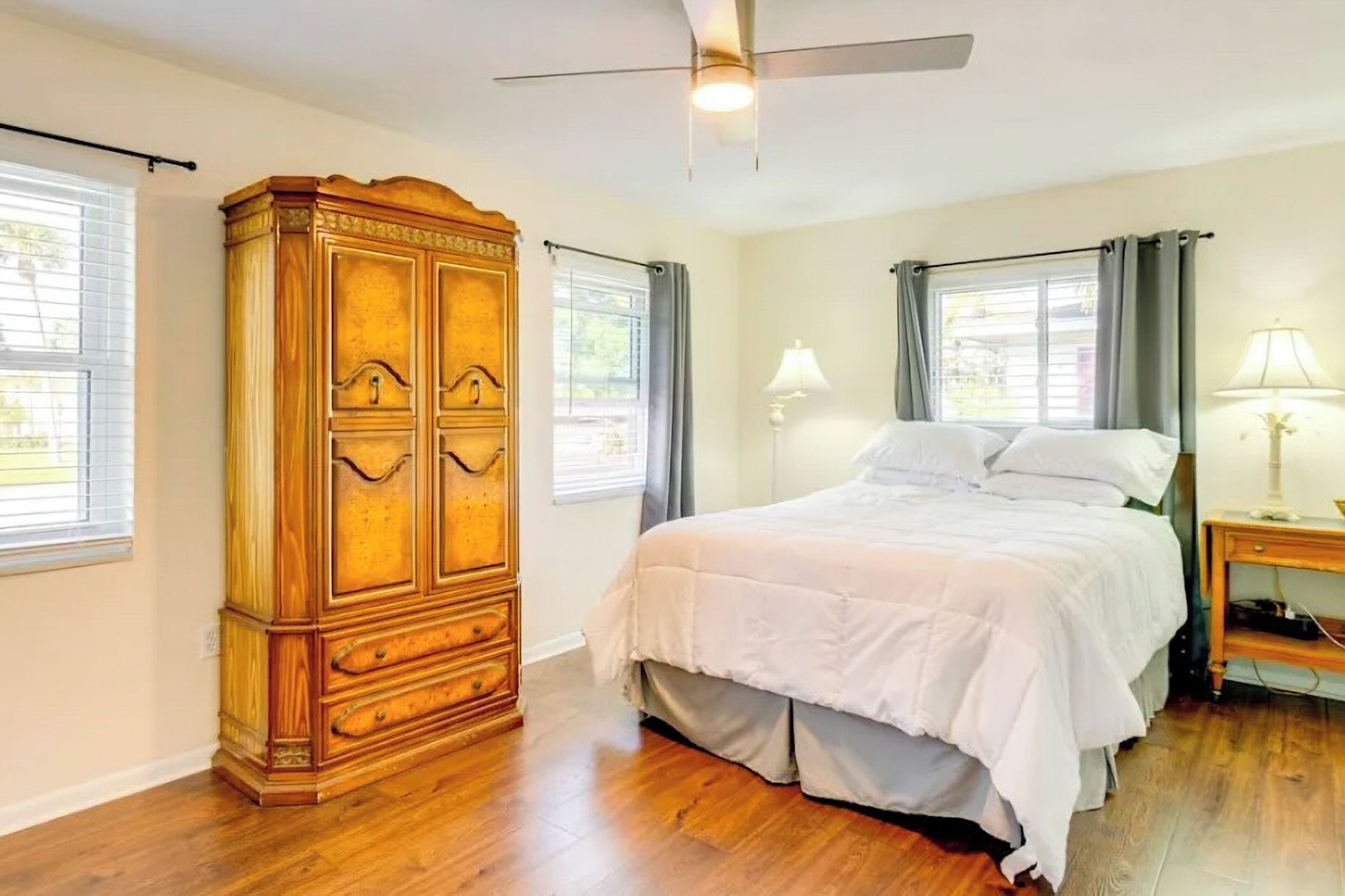 Camera da letto con un'armadio in legno, un letto con biancheria bianca, due abat-jour e una ventola a soffitto.