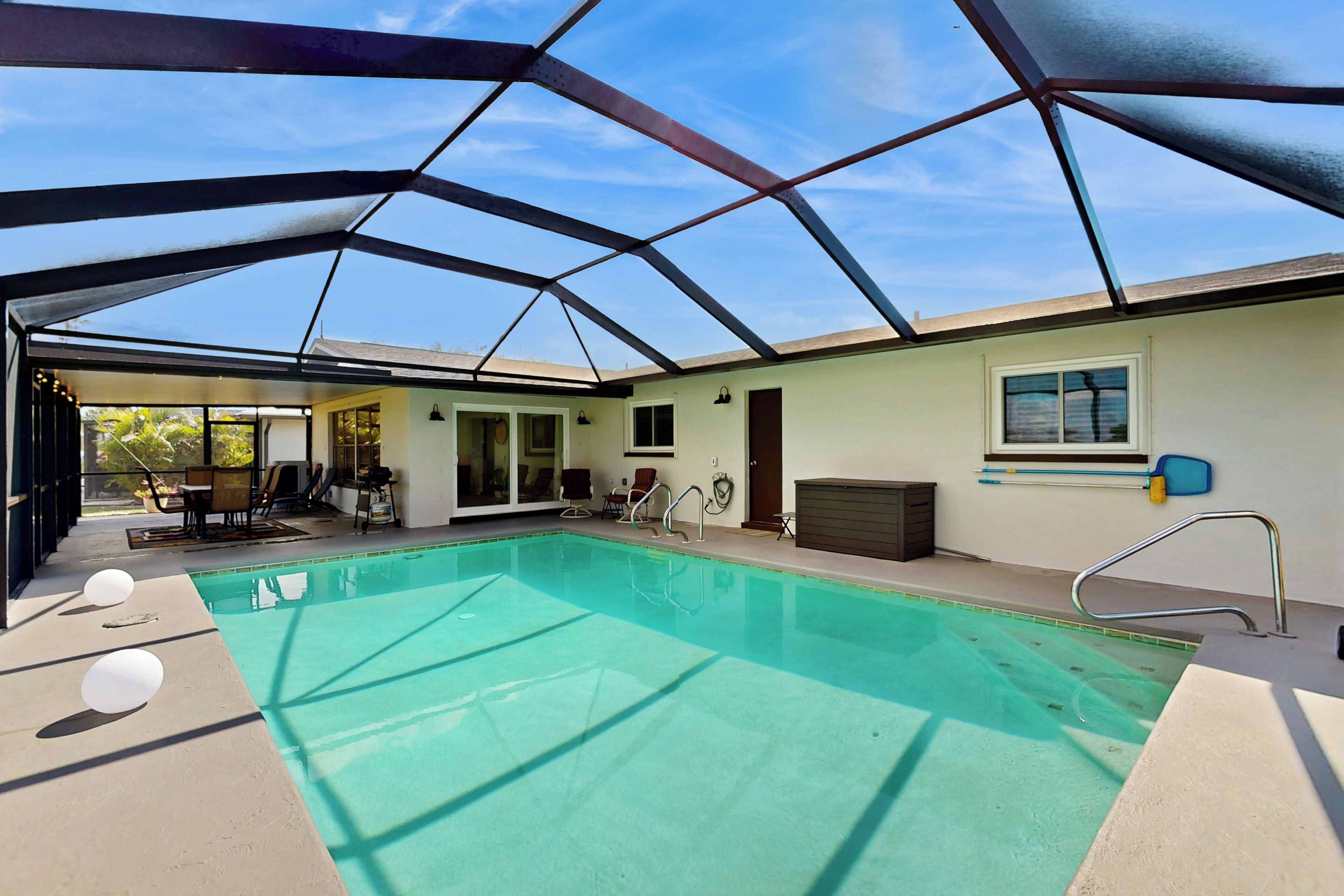 Une piscine intérieure couverte avec un toit en verre, un espace détente avec des fauteuils et une vue sur l’extérieur.