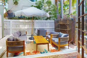 Un patio con mobiliario exterior, una cerca blanca y un paraguas grande.
