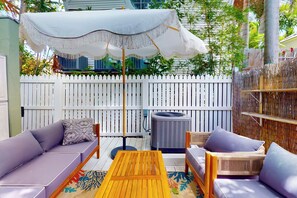 Un patio con un paraguas blanco, mobiliario de mimbre y una cerca blanca de piquetes.