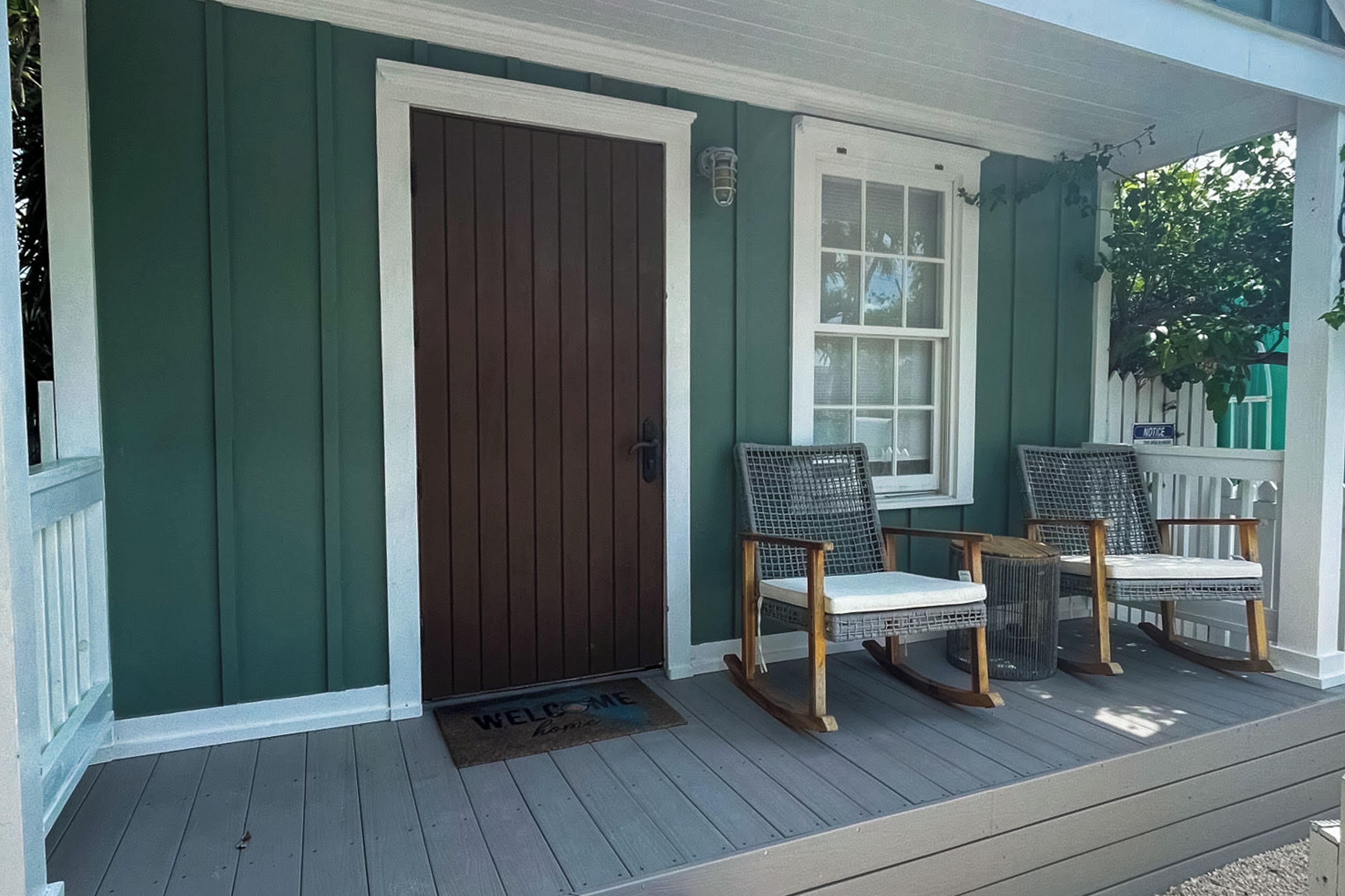 A porch with a dark brown door, two wicker rocking chairs, and a white window.