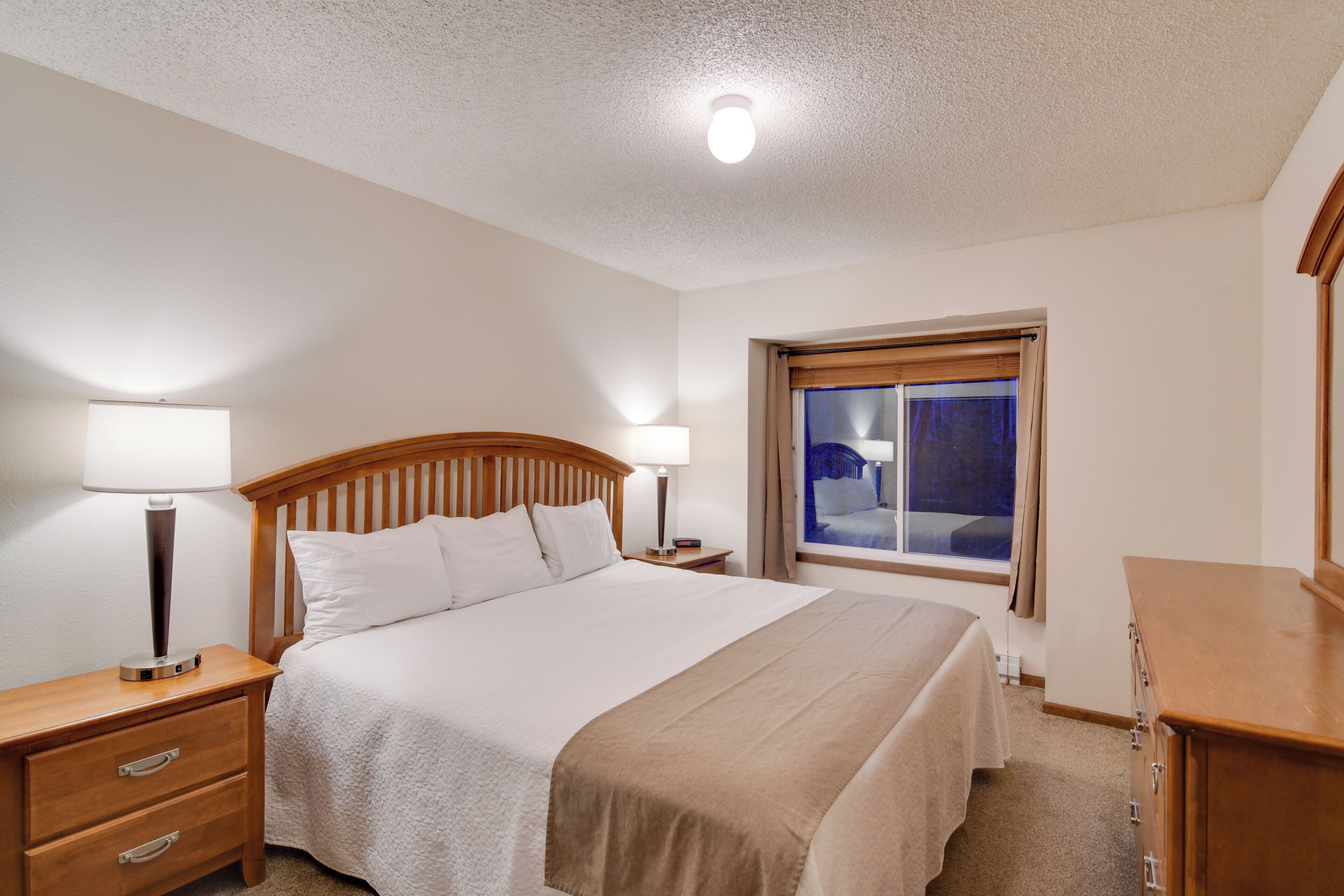 A neatly arranged bedroom with a single bed, bedside tables, a dresser, and a window with curtains.